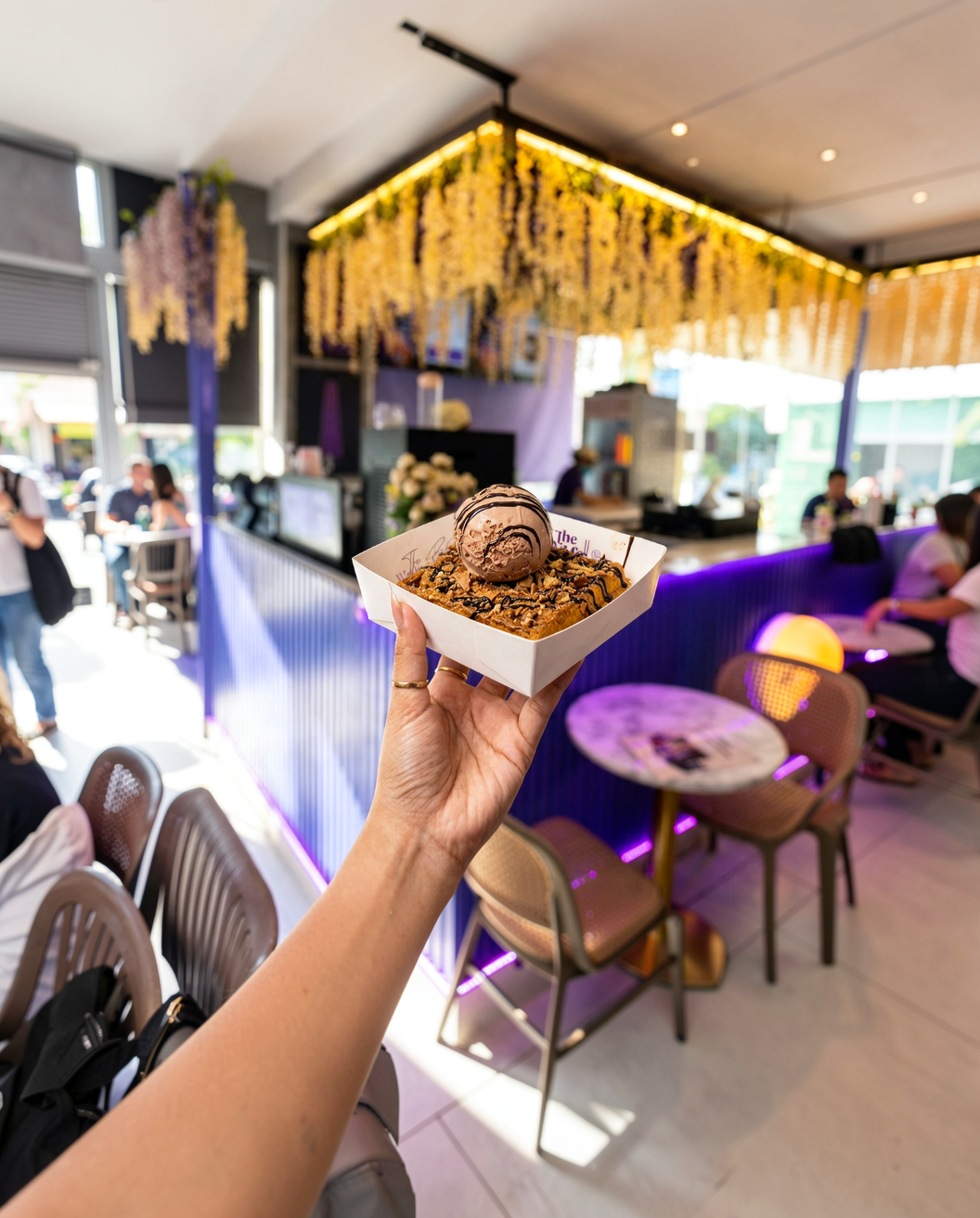 Hand holding a box of waffle bites topped with a chocolate ice-cream scoop inside The Wafflers café